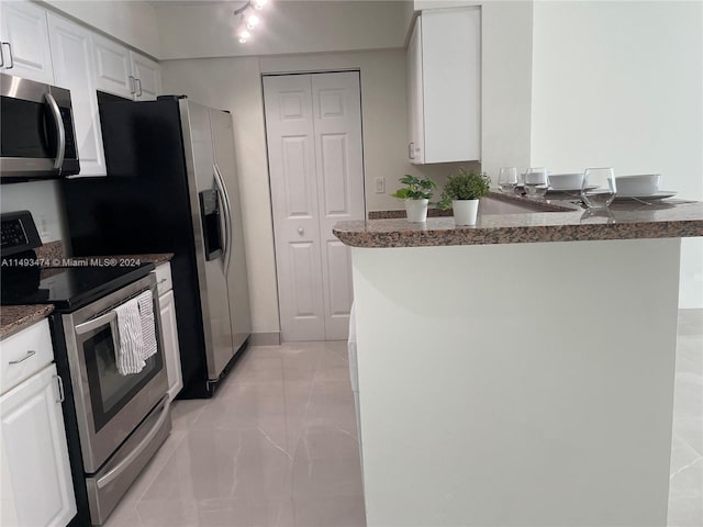 kitchen featuring white cabinets, light tile flooring, appliances with stainless steel finishes, and dark stone counters