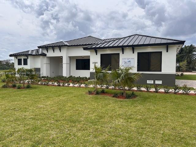 view of front facade featuring metal roof, stucco siding, a front lawn, and a standing seam roof