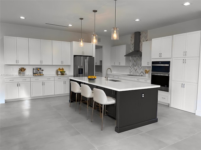 kitchen with multiple ovens, black electric stovetop, stainless steel fridge, wall chimney exhaust hood, and a sink