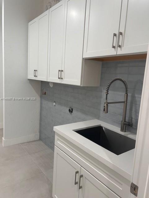 laundry room featuring a sink, baseboards, cabinet space, and light tile patterned floors