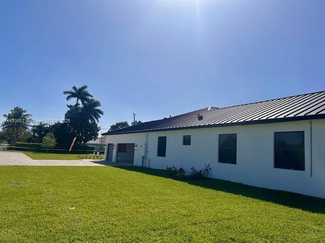 back of house with driveway, a standing seam roof, stucco siding, a lawn, and metal roof