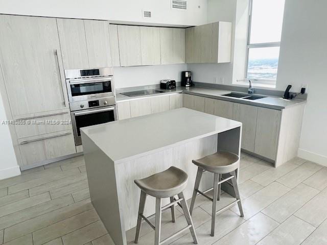 kitchen with stainless steel double oven, a kitchen bar, light hardwood / wood-style floors, black electric cooktop, and sink