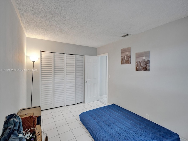 bedroom with light tile floors, a textured ceiling, and a closet