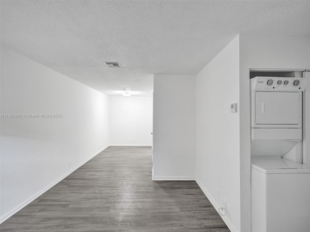 spare room with stacked washing maching and dryer, a textured ceiling, and dark hardwood / wood-style flooring