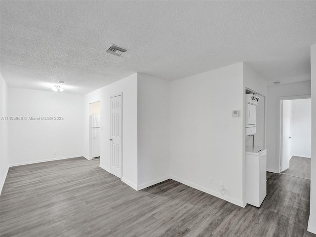 spare room featuring dark hardwood / wood-style floors, a textured ceiling, and stacked washer / drying machine