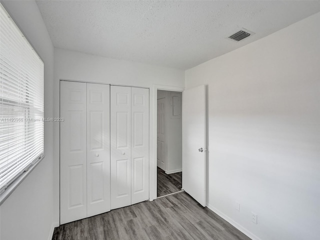 unfurnished bedroom featuring a closet, a textured ceiling, and dark hardwood / wood-style flooring