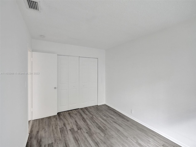 unfurnished bedroom featuring a textured ceiling, a closet, and hardwood / wood-style flooring