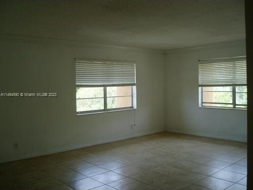 tiled empty room with ornamental molding and a healthy amount of sunlight