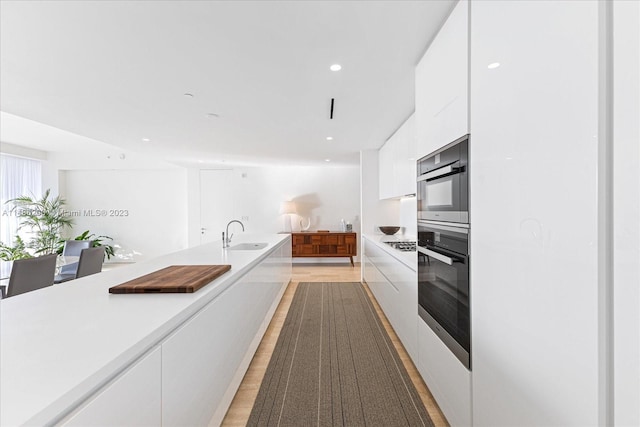 kitchen featuring sink, light wood-type flooring, multiple ovens, and white cabinetry