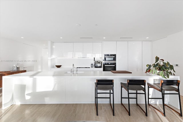 kitchen featuring white cabinetry, light wood-type flooring, sink, a breakfast bar area, and double oven