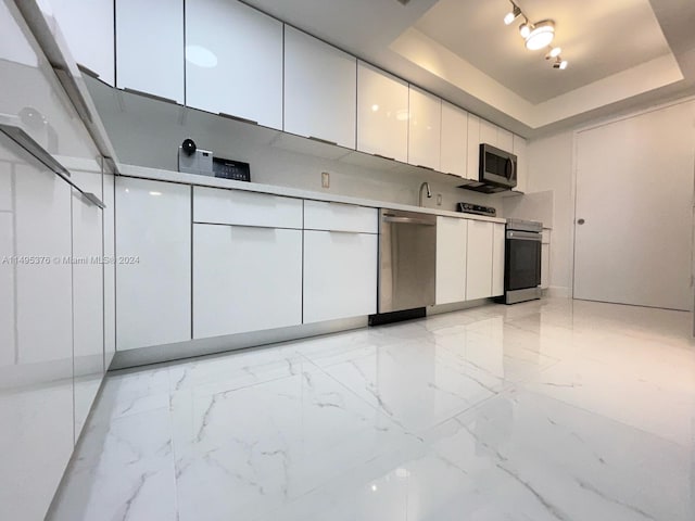 kitchen featuring white cabinetry, stainless steel appliances, track lighting, and a tray ceiling