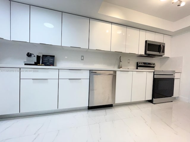 kitchen with stainless steel appliances, white cabinets, sink, light tile patterned flooring, and a raised ceiling