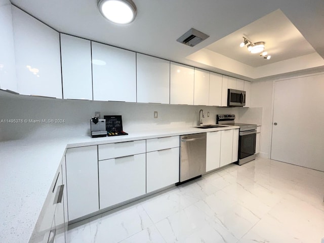 kitchen featuring light tile patterned floors, white cabinets, a tray ceiling, appliances with stainless steel finishes, and sink