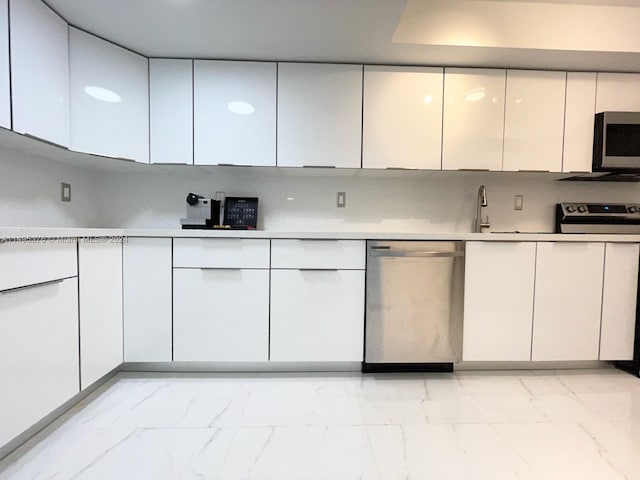 kitchen with appliances with stainless steel finishes, white cabinetry, sink, and light tile patterned flooring