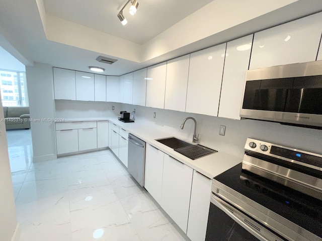 kitchen featuring light tile patterned flooring, white cabinetry, rail lighting, stainless steel appliances, and sink