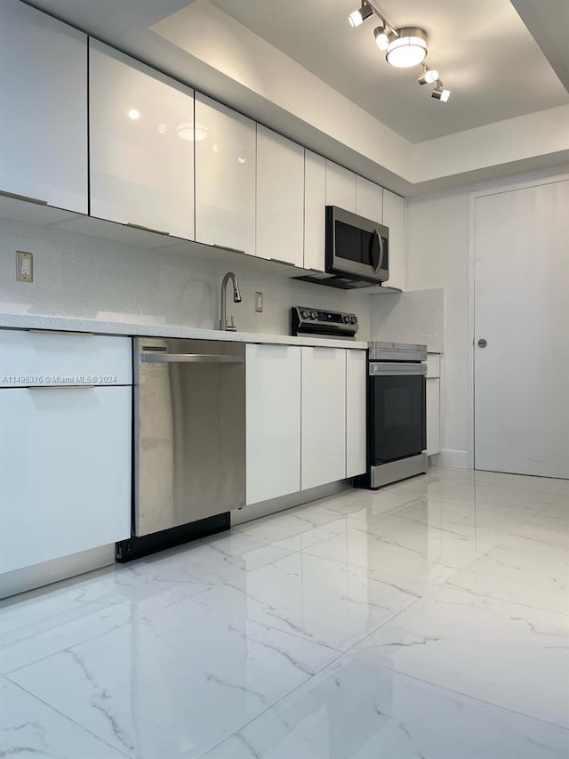 kitchen with appliances with stainless steel finishes, track lighting, light tile patterned floors, and white cabinets