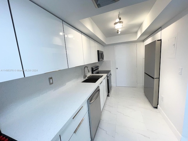 kitchen featuring stainless steel appliances, sink, light tile patterned floors, white cabinetry, and a raised ceiling