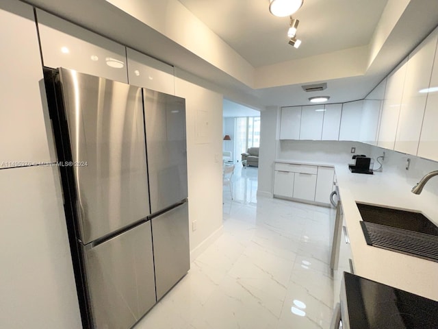 kitchen with light tile patterned flooring, a tray ceiling, white cabinets, and stainless steel fridge