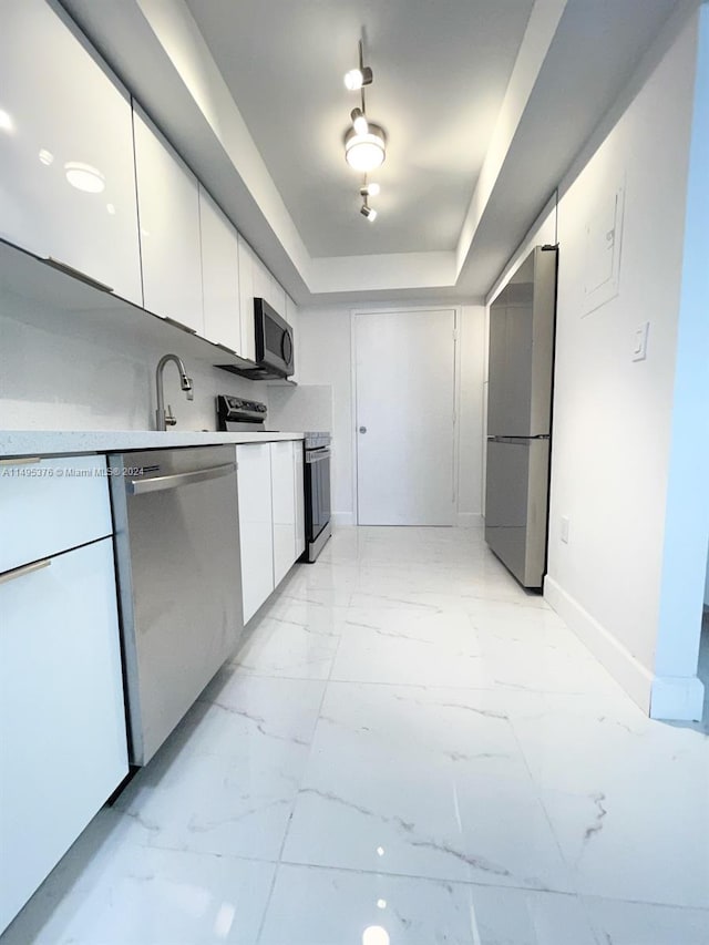 kitchen featuring white cabinetry, light tile patterned floors, a tray ceiling, stainless steel appliances, and sink