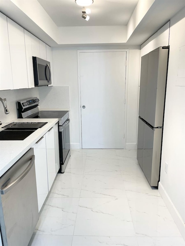 kitchen with light tile patterned flooring, white cabinetry, a tray ceiling, stainless steel appliances, and sink