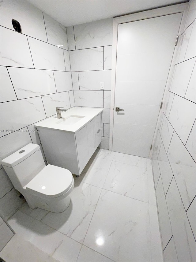 bathroom featuring tile patterned flooring, tile walls, toilet, and vanity