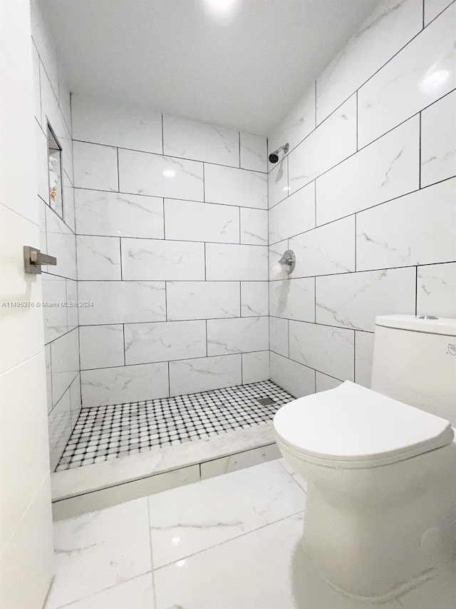 bathroom featuring tile patterned flooring, toilet, and tiled shower