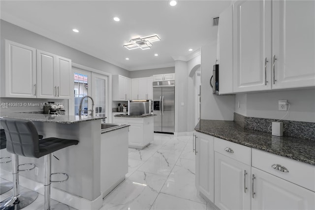 kitchen with dark stone counters, a center island, white cabinets, and stainless steel appliances