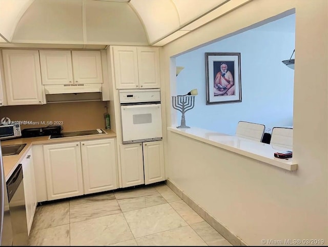 kitchen with black electric cooktop, light tile flooring, white cabinets, and oven