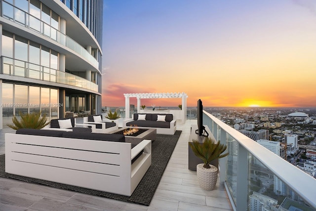 patio terrace at dusk featuring a balcony, a pergola, and an outdoor living space with a fire pit