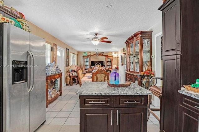 kitchen with a textured ceiling, stainless steel fridge with ice dispenser, light tile patterned flooring, a center island, and ceiling fan