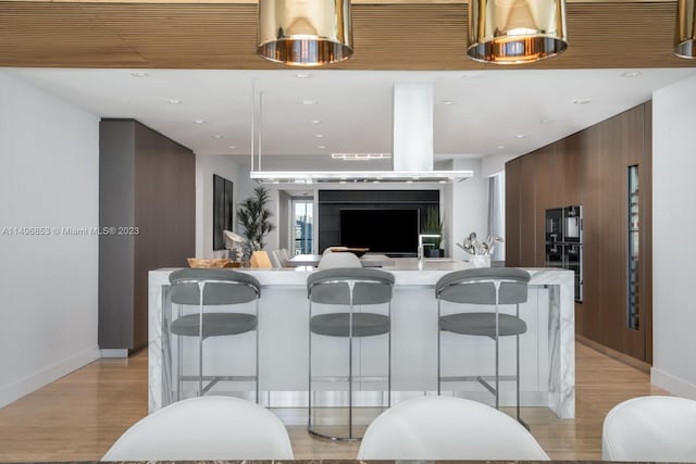 kitchen with a kitchen breakfast bar, light hardwood / wood-style floors, and an island with sink