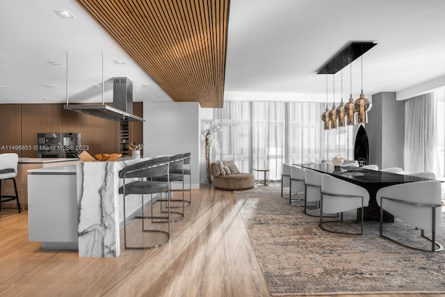 kitchen with pendant lighting, range hood, a breakfast bar area, a kitchen island, and light hardwood / wood-style flooring