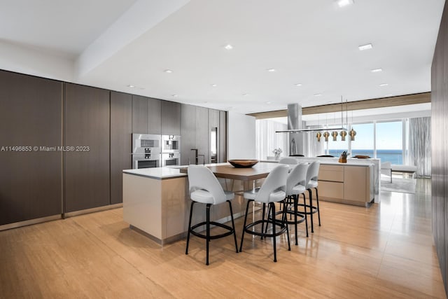 kitchen with a water view, a kitchen island with sink, light hardwood / wood-style floors, and decorative light fixtures