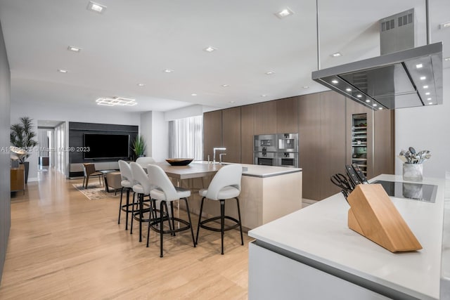 kitchen with light hardwood / wood-style floors, island exhaust hood, double oven, and a large island