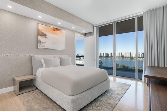 bedroom with a wall of windows, a water view, access to outside, and light wood-type flooring