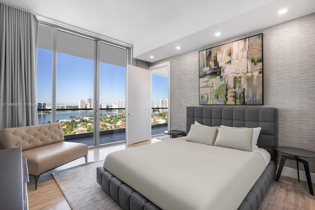 bedroom featuring floor to ceiling windows, a water view, access to exterior, multiple windows, and hardwood / wood-style floors