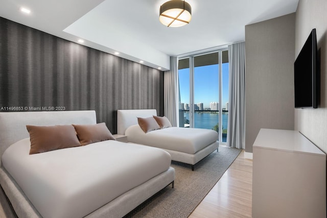 bedroom featuring access to exterior, a water view, expansive windows, and light wood-type flooring