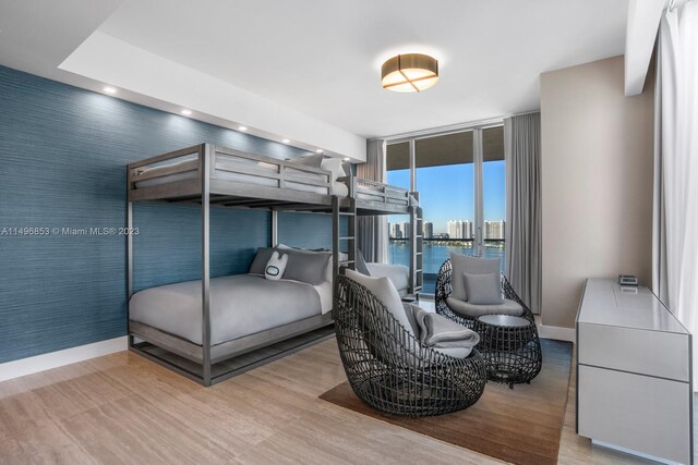 bedroom featuring light wood-type flooring, a water view, and expansive windows