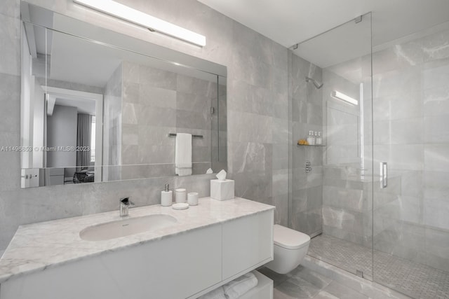 bathroom with tile walls, a shower with shower door, toilet, and vanity