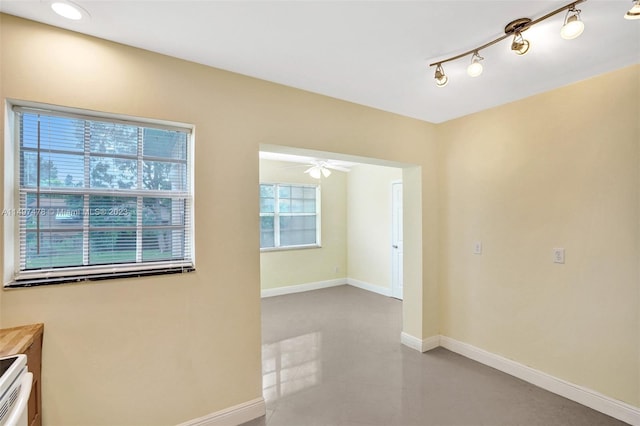 empty room featuring track lighting, ceiling fan, and a healthy amount of sunlight