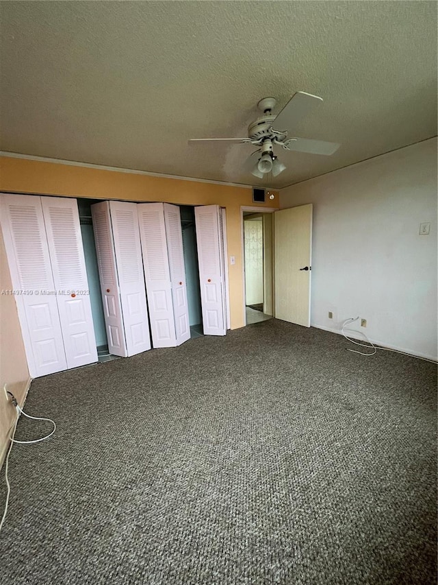 unfurnished bedroom featuring ceiling fan, dark carpet, and a textured ceiling