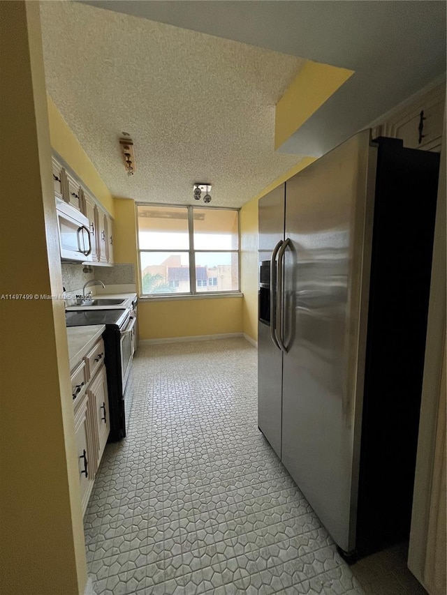 kitchen featuring a textured ceiling, stainless steel fridge, white cabinetry, and sink