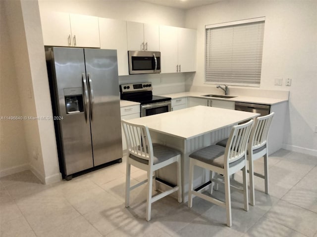 kitchen with a kitchen breakfast bar, white cabinetry, stainless steel appliances, light tile floors, and sink