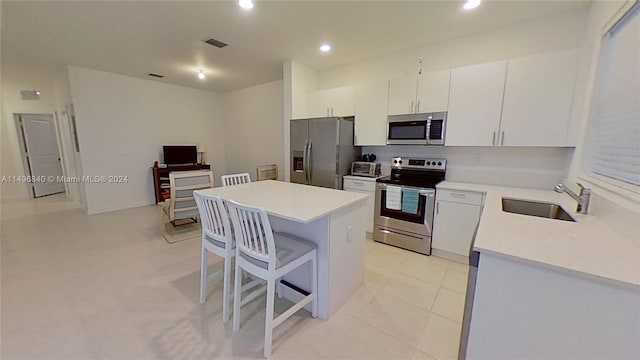 kitchen with a breakfast bar area, stainless steel appliances, white cabinetry, sink, and a center island