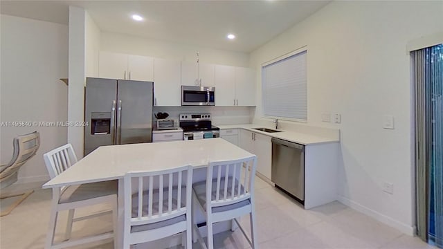 kitchen with appliances with stainless steel finishes, a kitchen island, a kitchen bar, light tile flooring, and white cabinetry