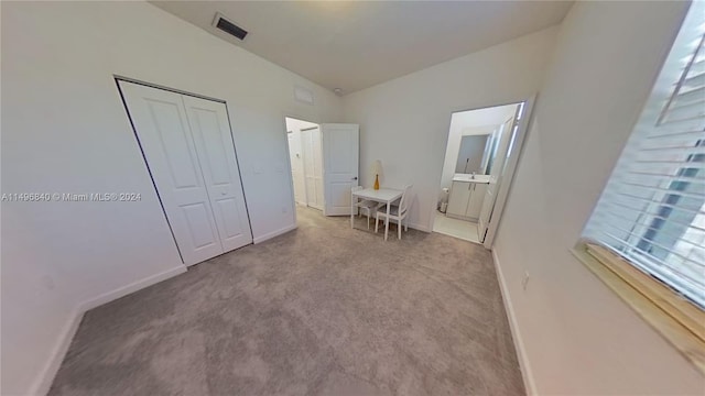 unfurnished bedroom featuring connected bathroom, light carpet, a closet, and lofted ceiling