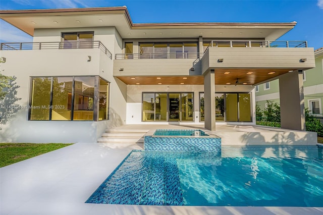 rear view of property featuring a balcony, a patio area, a pool with connected hot tub, and stucco siding