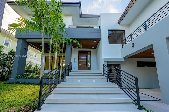 entrance to property with a yard, a balcony, and stucco siding