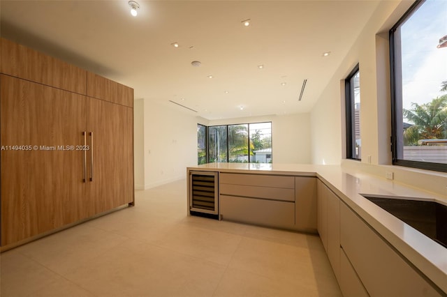 kitchen featuring modern cabinets, wine cooler, a peninsula, light countertops, and a sink