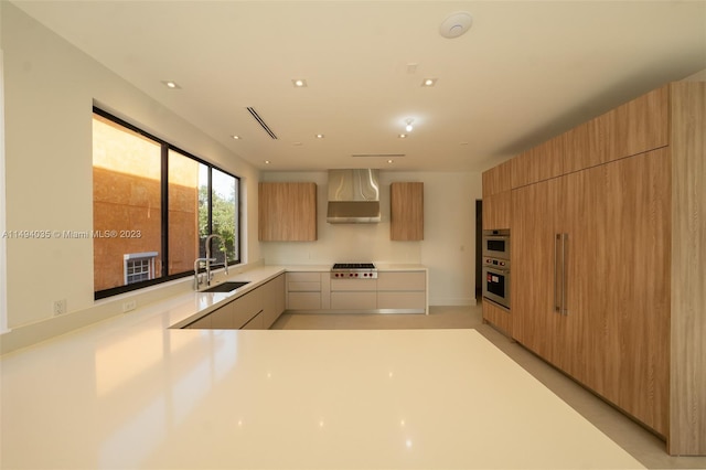 kitchen featuring stainless steel appliances, light countertops, a sink, wall chimney range hood, and modern cabinets